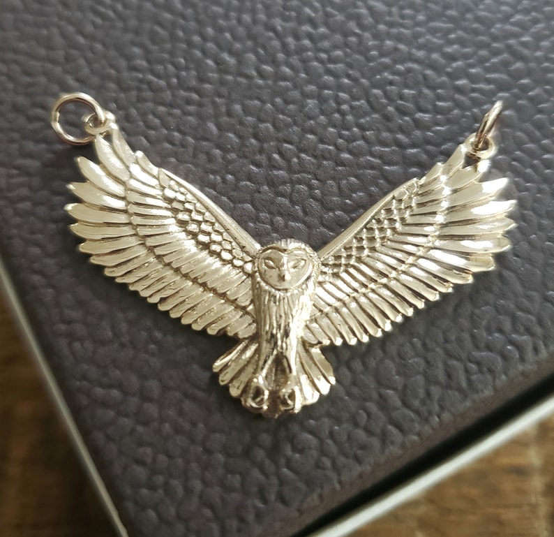 May include: A gold-toned owl pendant with outstretched wings. The owl is detailed with feathers and has a realistic appearance.