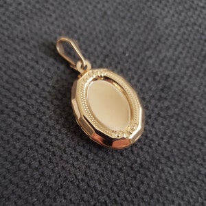 May include: A gold oval locket pendant with a detailed engraved border. The locket is closed and ready to hold a special memory.