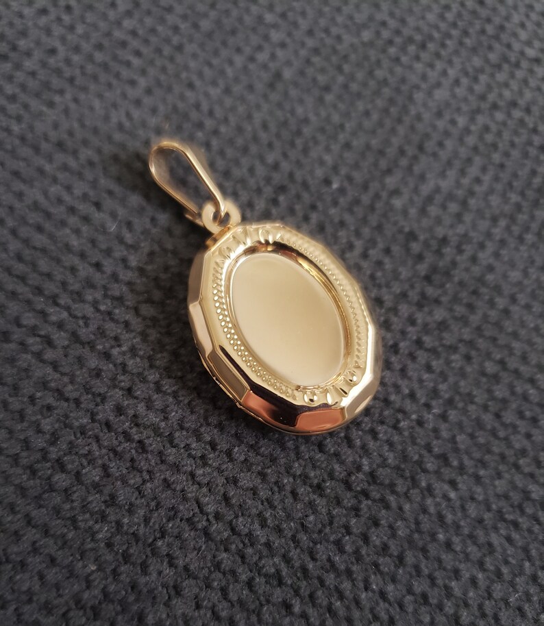 May include: A gold oval locket pendant with a detailed engraved border. The locket is closed and ready to hold a special memory.