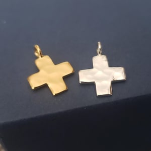 May include: Two hammered metal cross charms, one gold and one silver. The charms are both in the shape of a plus sign and have a textured surface.