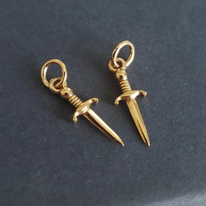 May include: Two gold-toned dagger charms with a loop at the top for attaching to a necklace or bracelet.
