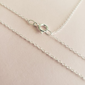 May include: A silver chain necklace with a lobster clasp closure. The chain is made of small, oval-shaped links.