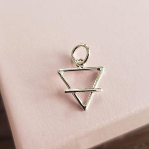 May include: Silver charm pendant featuring a triangle with a horizontal line through the center. The charm is designed in a minimalist style and has a simple, elegant look.