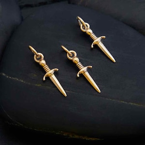 Peut inclure: Trois breloques en forme de poignard dor&eacute;es avec un design d&eacute;taill&eacute;. Les breloques sont petites et d&eacute;licates, parfaites pour ajouter une touche de fantaisie &agrave; vos bijoux.