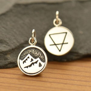 May include: Two silver charms, one with a mountain range design and the other with a triangle and line symbol.