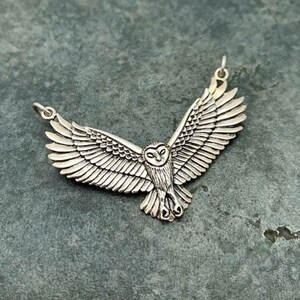 May include: A silver owl pendant with outstretched wings. The owl is detailed with feathers and has a realistic appearance.