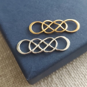 May include: Two infinity symbol charms, one gold and one silver, on a blue background.