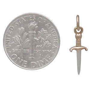 Peut inclure: Un charme en forme de dague argent&eacute;e avec une poign&eacute;e dor&eacute;e. Le charme est pr&eacute;sent&eacute; &agrave; c&ocirc;t&eacute; d'une pi&egrave;ce de dix cents am&eacute;ricaine pour comparaison de taille.