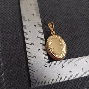 May include: A gold oval locket pendant with a detailed engraved design. The locket is approximately 1.5 inches in length.