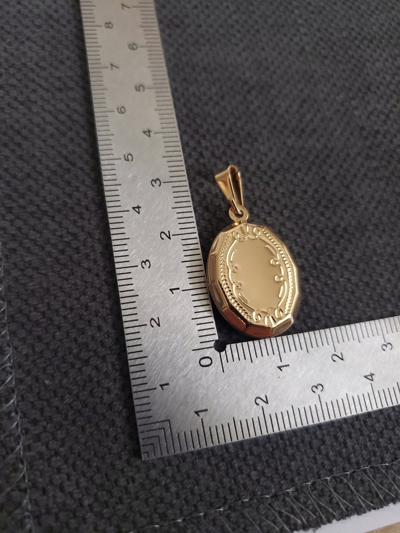 May include: A gold oval locket pendant with a detailed engraved design. The locket is approximately 1.5 inches in length.