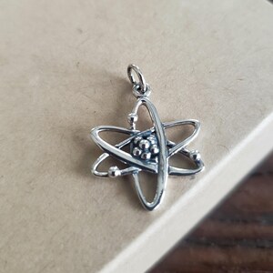 May include: A silver atom charm pendant with a detailed design of a nucleus and orbiting electrons.