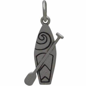 K&ouml;nnte beinhalten: Ein silberfarbener Anh&auml;nger mit einem Stand-Up-Paddleboard und Paddel. Das Paddleboard hat ein dekoratives Wirbeldesign und eine geometrische Form am unteren Ende. Der Anh&auml;nger ist zum Anbringen an einer Halskette oder einem Armband gedacht.