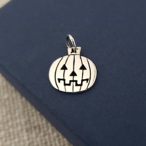 May include: A silver charm in the shape of a jack-o'-lantern with a carved face.