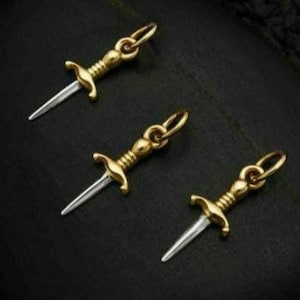 May include: Three gold-colored dagger charms with a silver blade. The charms are hanging from a loop at the top.