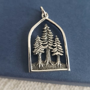 May include: A silver pendant in the shape of an archway with three stylized trees inside. The pendant is a detailed, three-dimensional design.