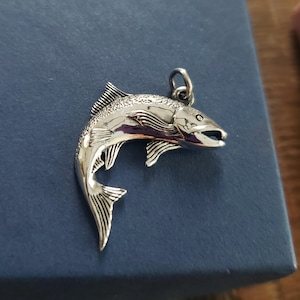 May include: A silver charm in the shape of a leaping salmon. The charm is detailed with scales and fins.