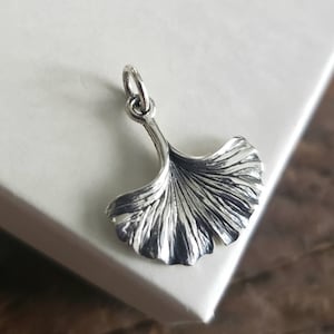 May include: A silver charm in the shape of a ginkgo leaf. The leaf is detailed with veins and has a smooth, polished finish.
