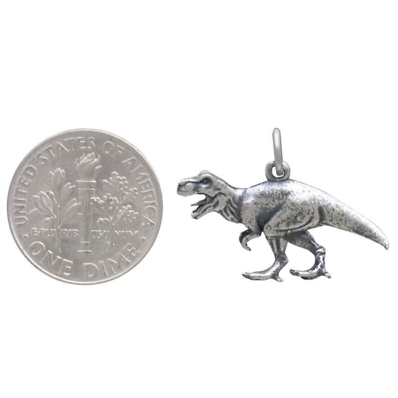 May include: A silver-toned Tyrannosaurus Rex dinosaur charm pendant, shown next to a US dime for size comparison.
