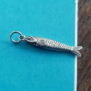 May include: A silver-colored fish pendant with detailed scales, fins, and a loop for a chain. The pendant is a small, detailed representation of a fish, perfect for jewelry or crafting projects.