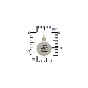 May include: A round silver charm featuring a black engraved swimmer icon, positioned against a measurement scale showing a diameter of approximately 0.5 inches. The charm includes a small circular jump ring at the top for attachment.