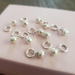 May include: A collection of silver charm pendants with white pearl accents. Each pendant features a small silver ring and two white pearls.
