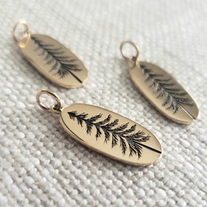 May include: Three gold oval-shaped charms with a black silhouette of a pine tree etched on each charm.