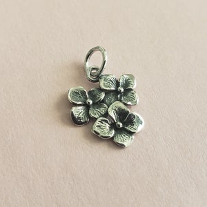 Peut inclure: Breloque en argent représentant trois fleurs d'hortensia en trois dimensions. Le breloque a une boucle en haut pour l'attacher à un bracelet ou un collier.