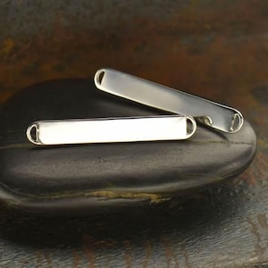 May include: Two silver metal bar tags with rounded edges and holes at each end. The tags are blank and ready for personalization.