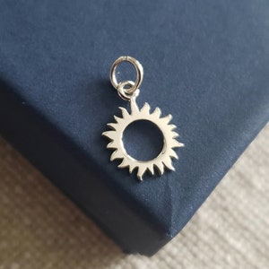 Puede incluir: Un dije de sol de plata con un diseño circular y un bucle para sujetarlo a un collar o pulsera.