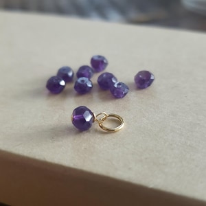 May include: A close-up of a gold charm with a purple amethyst gemstone. The charm is surrounded by several other amethyst gemstones.
