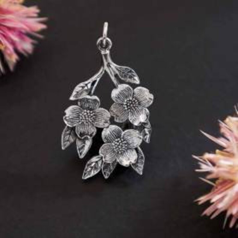 May include: Silver pendant featuring a delicate branch with three stylized flowers and leaves.