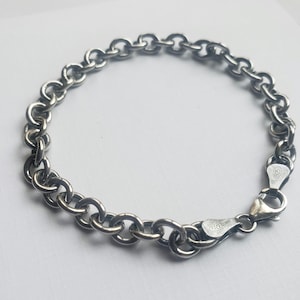 May include: A silver-colored bracelet with a series of interconnected, rounded links. The bracelet features a lobster clasp closure. The links are evenly spaced, creating a continuous chain. The bracelet is likely made of metal.
