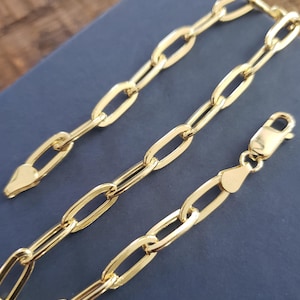 May include: A gold chain bracelet with a lobster clasp closure. The chain is made of oval-shaped links.