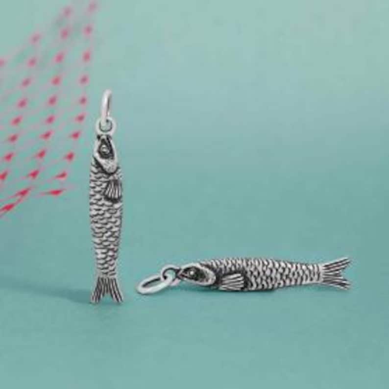 May include: Two silver fish charms. One charm is upright, the other is lying down. The fish have detailed scales, fins, and eyes. The charms are designed to be used as pendants or additions to a bracelet.