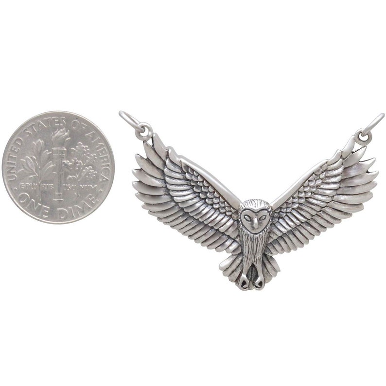 May include: Silver owl pendant necklace with outstretched wings. The owl is detailed with feathers and has a realistic appearance. The pendant is about the size of a US dime.