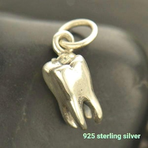 May include: A silver-colored molar charm with a loop for a necklace or bracelet. The charm is made of 925 sterling silver and has detailed grooves and contours. The text "925 sterling silver" is visible at the bottom.