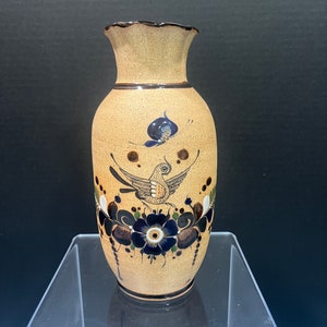 May include: A tan ceramic vase with a scalloped rim, decorated with a blue and brown bird, flowers, and leaves. The vase has a brown glaze and is hand-painted.