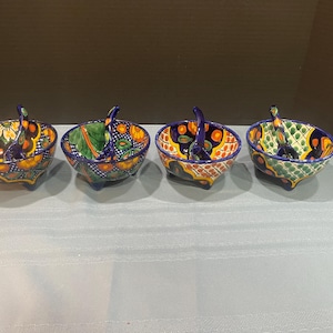 May include: Four hand-painted ceramic bowls with handles and spoons. Each bowl has a unique design with vibrant colours including blue, yellow, orange, and green. The bowls are likely for serving dips or sauces.