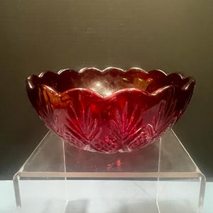 May include: A deep red glass bowl featuring a scalloped rim and a pressed diamond pattern on the exterior. The bowl has a translucent quality with a glossy finish, showcasing a repeating geometric design that radiates from the base to the edge.