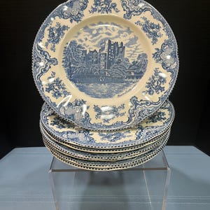 May include: A stack of five round ceramic plates featuring a blue and white transferware pattern. The center of each plate depicts a castle scene with the text Blarney Castle, Ireland. The rim has a decorative floral and scroll border design.