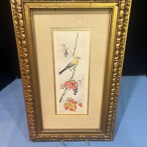 May include: A framed print of a yellow bird perched on a vine with red and purple grapes. The print is in a gold frame with a textured border.