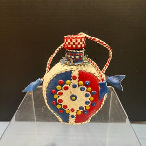 May include: A small, round, white leather bottle with a red, white, and blue checkered top. The bottle is decorated with blue, red, and yellow circles.