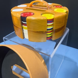 May include: A wooden poker chip set with a handle. The set is round and has slots for different colored chips, including red, white, yellow, and blue. The case is made of light brown wood and has a matching handle.