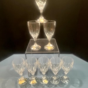 May include: A collection of clear crystal wine glasses. The glasses are arranged in a pyramid shape, with a single champagne flute at the top. The bases of the glasses have a gold accent.