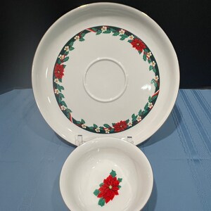 May include: A white ceramic serving platter with a gold rim and a Christmas-themed design featuring poinsettia flowers, holly leaves, and white berries. A smaller white ceramic bowl with a gold rim and a single poinsettia flower design is also included.
