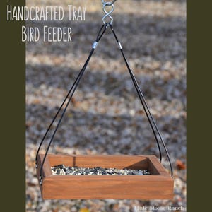 May include: Handcrafted wooden bird feeder tray, suspended by black wires from a metal ring. The tray is filled with birdseed. Text on the image reads "Handcrafted Tray Bird Feeder" and "Little Moose Ranch".
