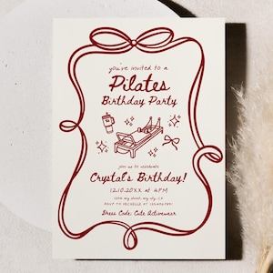 May include: A Pilates birthday party invitation with a burgundy frame and text. The invitation includes illustrations of Pilates equipment and a coffee cup. A fluffy, beige plant stem is in the background.