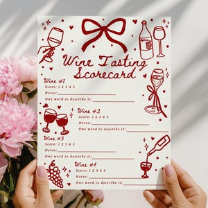 May include: A wine tasting scorecard with red illustrations and text, held in front of a bouquet of pink peonies. The scorecard includes spaces for wine notes and scores, with the title "Wine Tasting Scorecard".