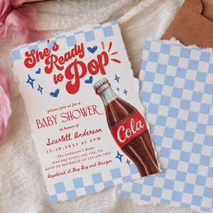 Puede incluir: Invitaci&oacute;n a baby shower con el texto "She's Ready to Pop" en escritura roja. La invitaci&oacute;n presenta una ilustraci&oacute;n de botella de cola y detalles a cuadros azules. Incluye detalles del evento e informaci&oacute;n RSVP.