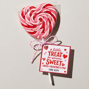 May include: A heart-shaped lollipop with red and pink swirls, wrapped in clear cellophane. A small tag reads "a little TREAT for someone SWEET Happy Valentine's Day! From Olivia" tied with pink and white string.